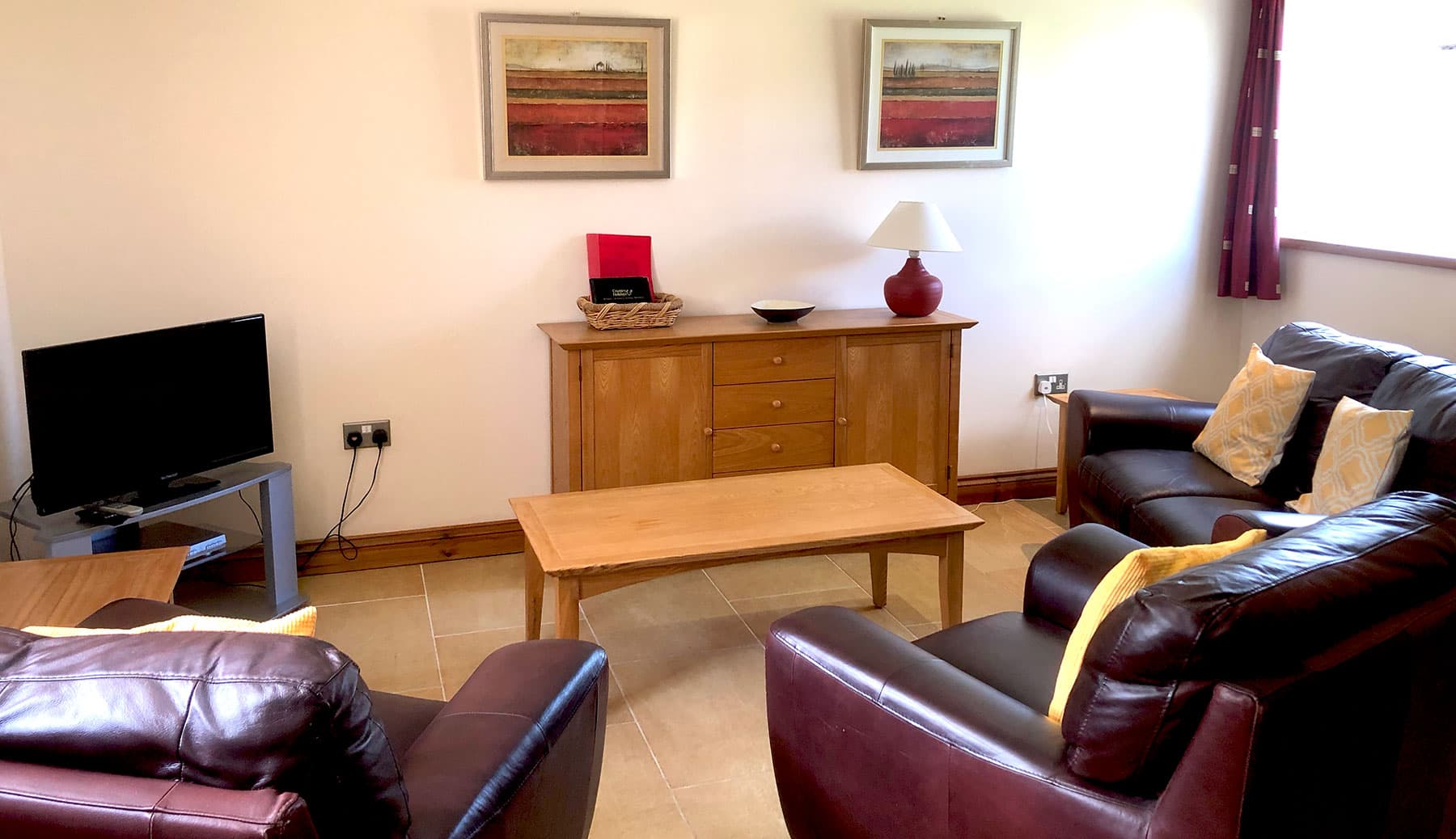 Sitting room with brown leather sofas, a coffee table, a TV and an oak sideboard beneath two paintings of poppy fields