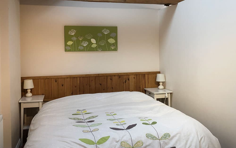 Double bed with leaf-patterned bedding and a wooden headboard, between white bedside tables with lamps