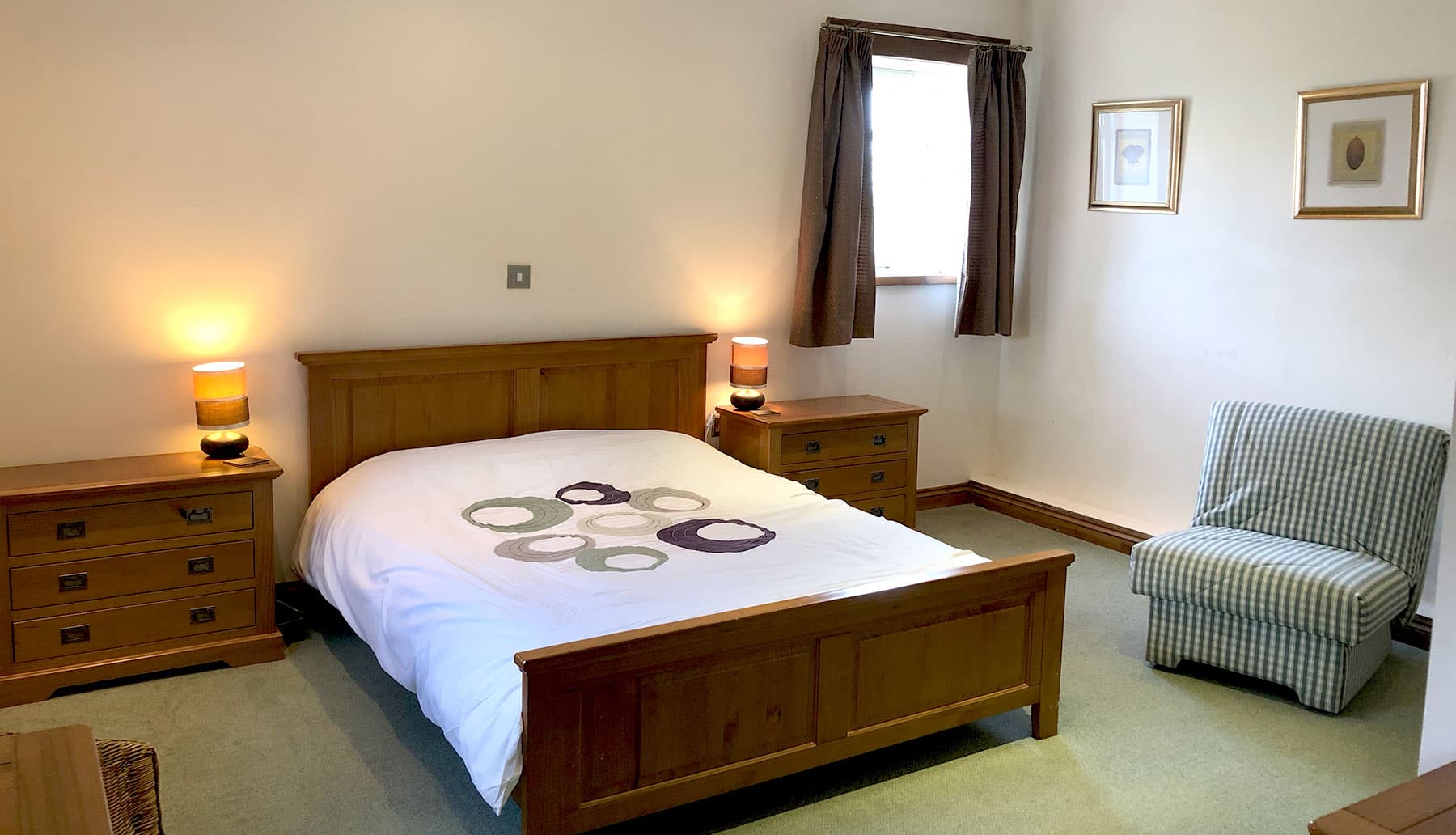 Double bedroom with an oak bed, oak bedside chests with lamps and a checked armchair