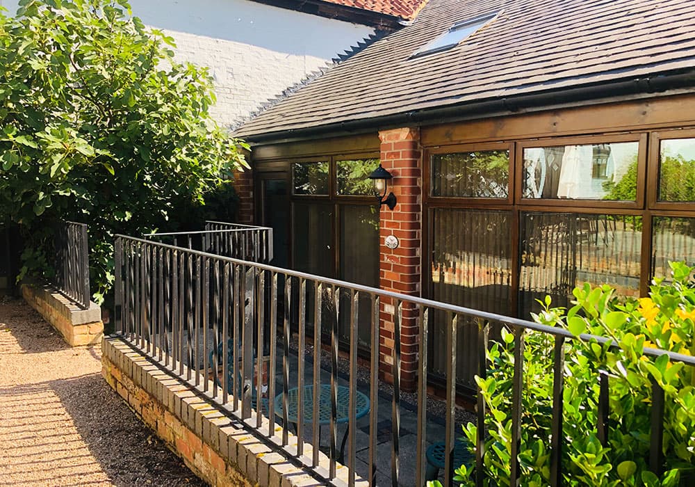 Brick and timber cottage with a glazed frontage behind black railings and shrubs
