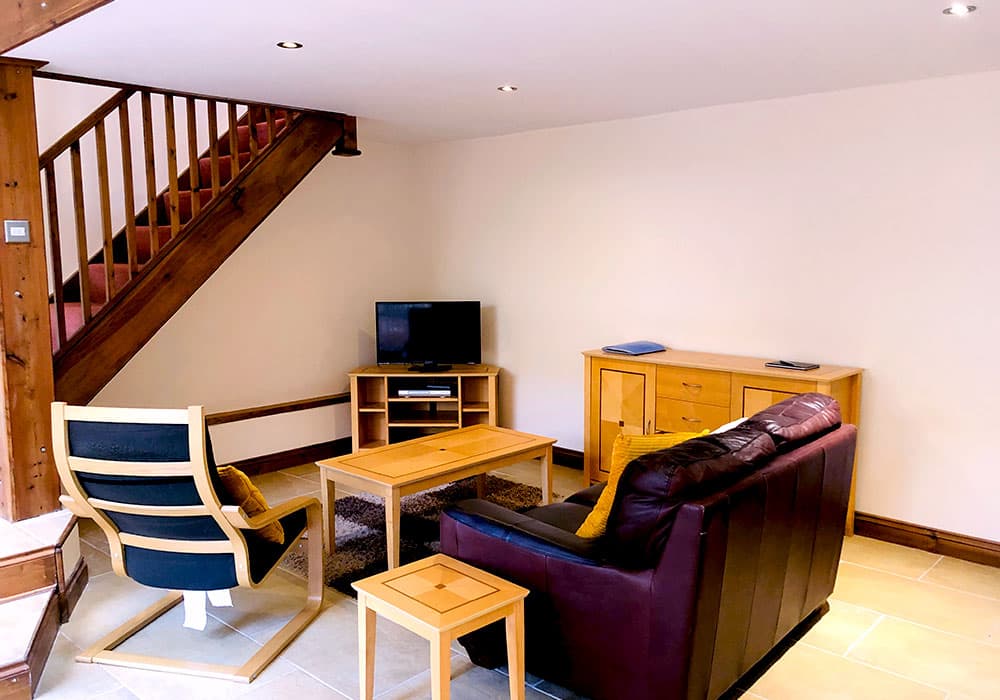 Living room with a leather sofa, armchair, coffee table and TV at the foot of a wooden staircase