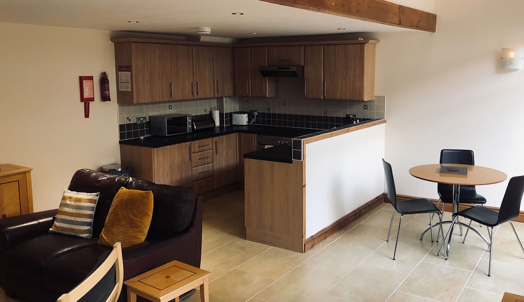 Open-plan room with a leather sofa, a round dining table with two chairs and a kitchen with oak units