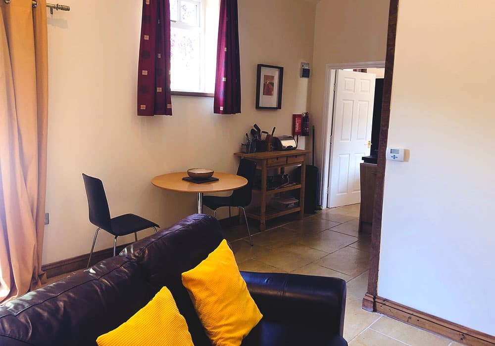 Living area with a leather sofa with yellow cushions and a small round dining table with two chairs