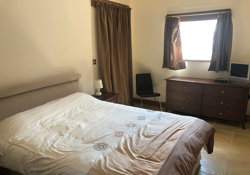 Bedroom with a double bed, a dark chest of drawers and a chair by the window