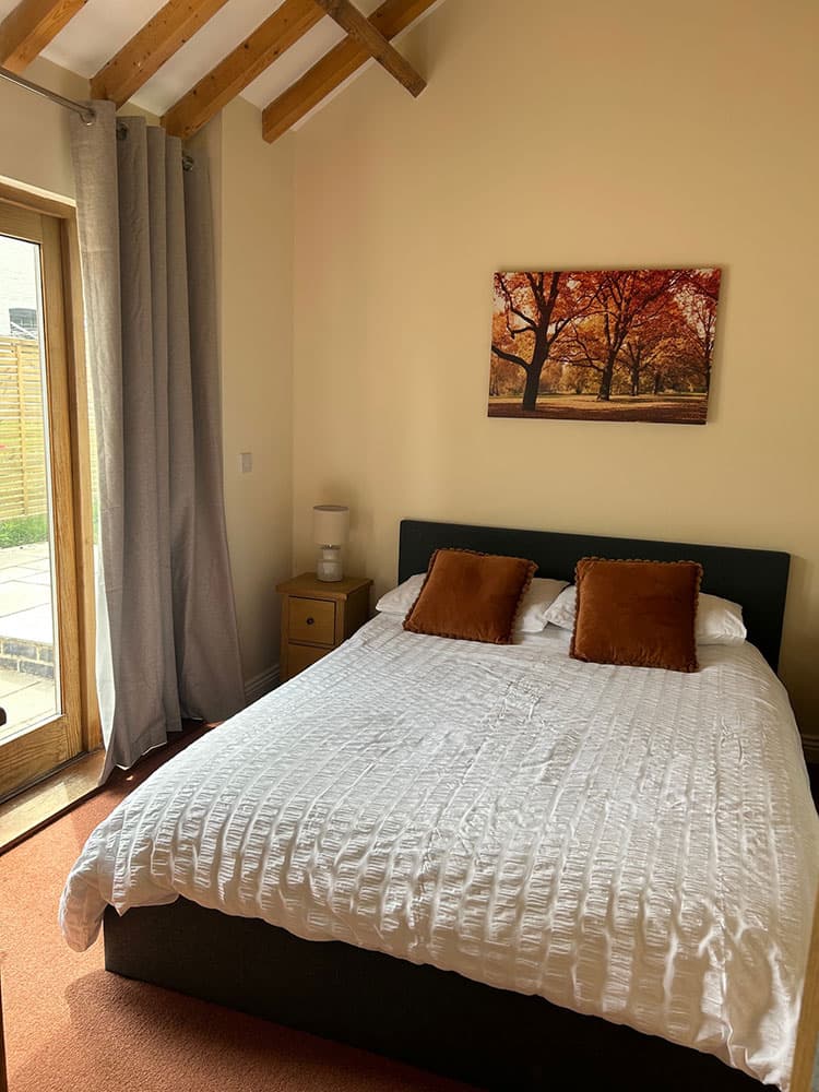 Double bed with white bedding and rust-coloured cushions beside a glazed door