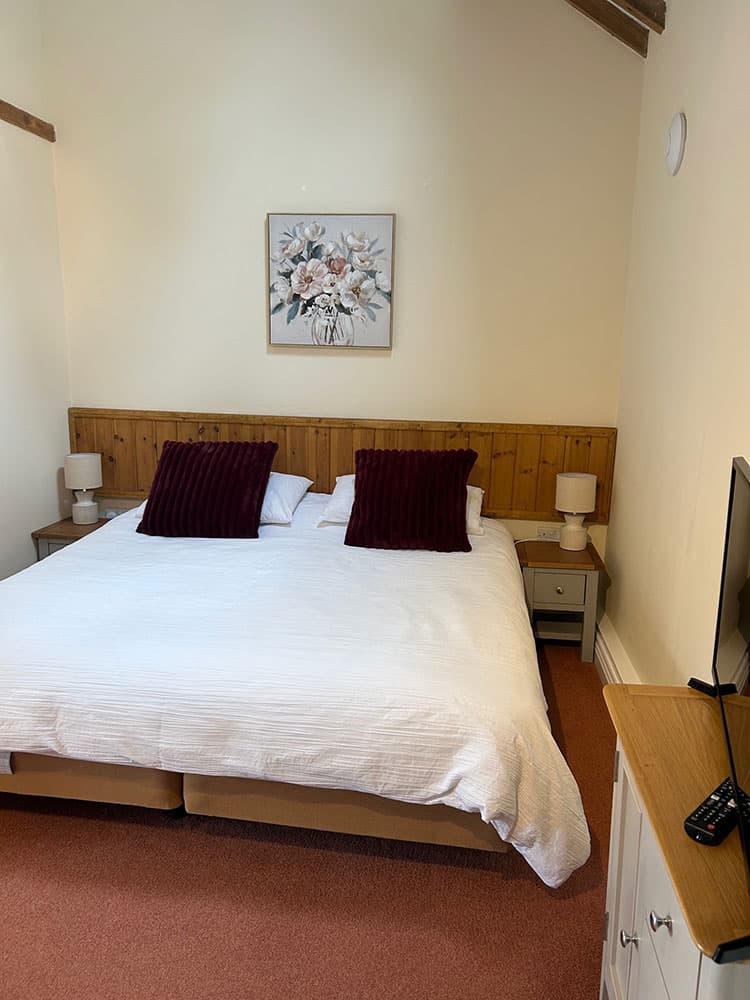 Large bed with white bedding and burgundy cushions beneath a floral picture